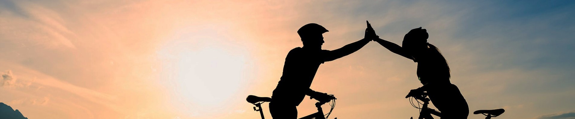 Two cyclists with raised arms with light shining 
towards the viewer